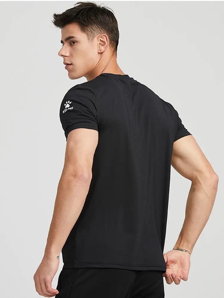 A man wearing a black short-sleeve athletic t-shirt with a white Kari Traa logo on the left sleeve, shown from a three-quarters back view against a light gray background.
