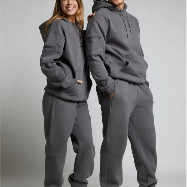 Two people wearing matching gray hoodie and pants sets on a plain background