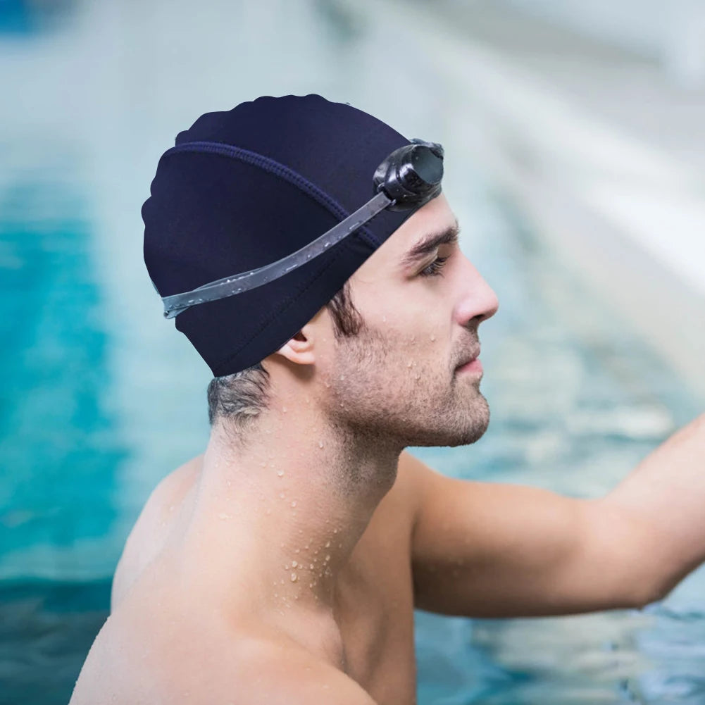 Man wearing a navy swim cap with goggles on his head, standing by a pool.