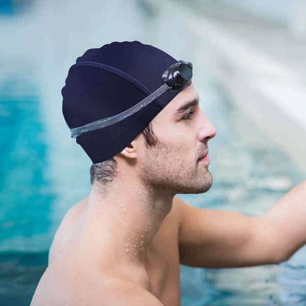 Man wearing a navy swim cap with goggles on his head, standing by a pool.