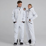 Two people wearing white ski suits on a gray background