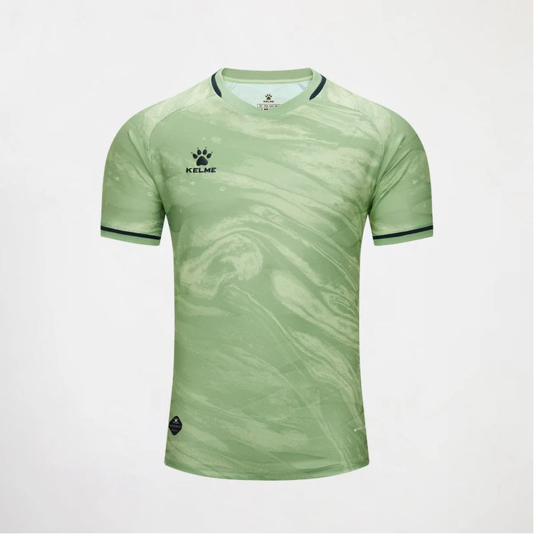 A light green short-sleeve soccer jersey with a subtle marbled pattern, featuring the KELME logo on the left chest and dark green trim on the collar and sleeve cuffs, displayed against a light gray background.
