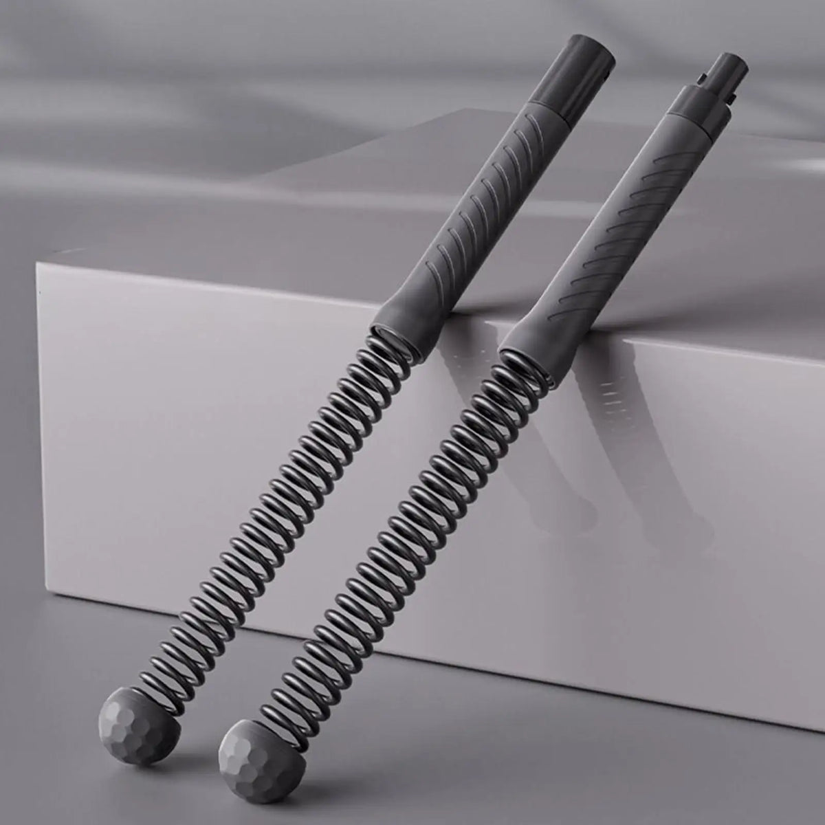 Two gray spring-loaded tools on a reflective surface with a neutral background