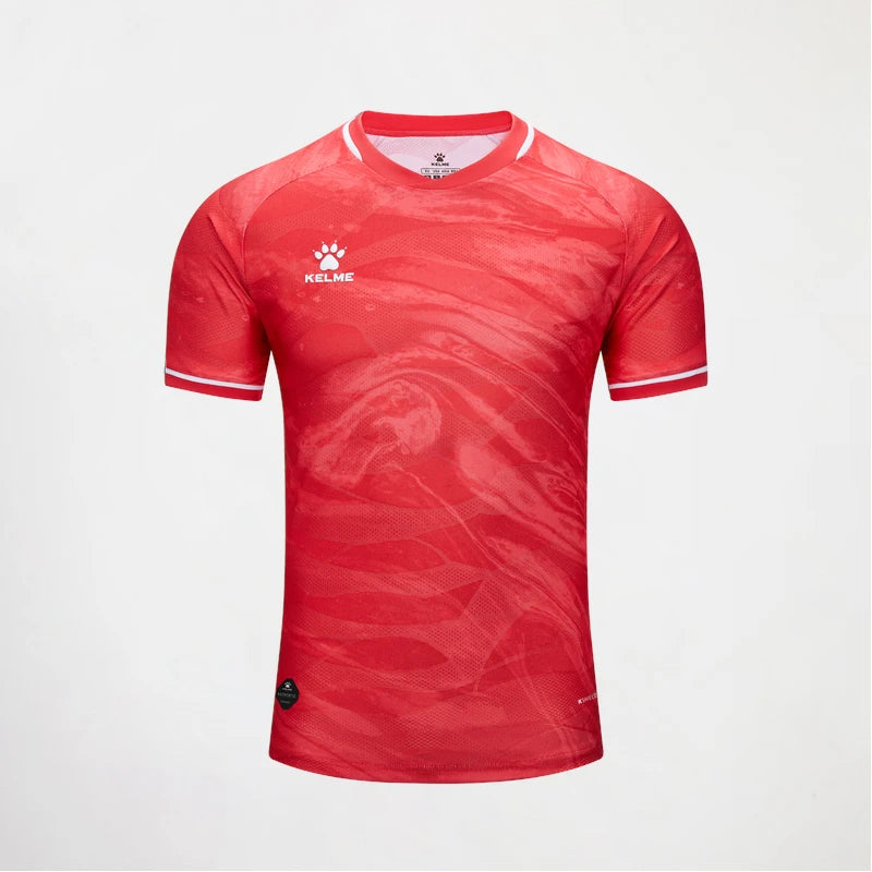 A red short-sleeve athletic jersey with a subtle tonal wavy pattern, featuring the KELME logo on the left chest and white trim on the collar and sleeve cuffs, displayed against a light gray background.