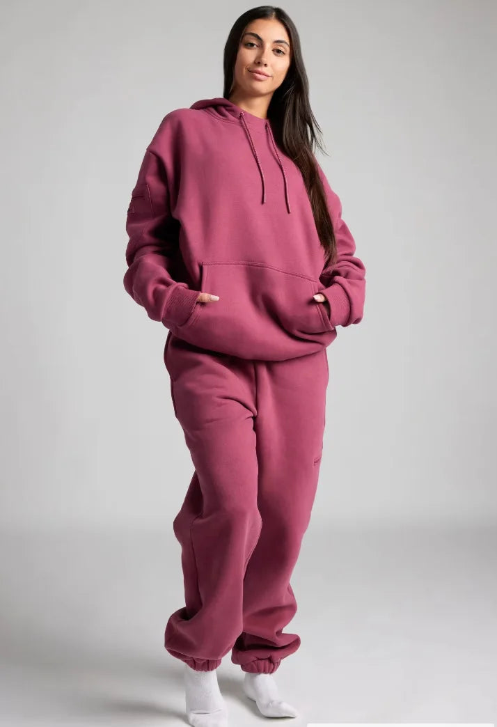 Person wearing a pink hoodie and pants set on a gray background