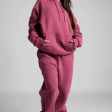Person wearing a pink hoodie and pants set on a gray background