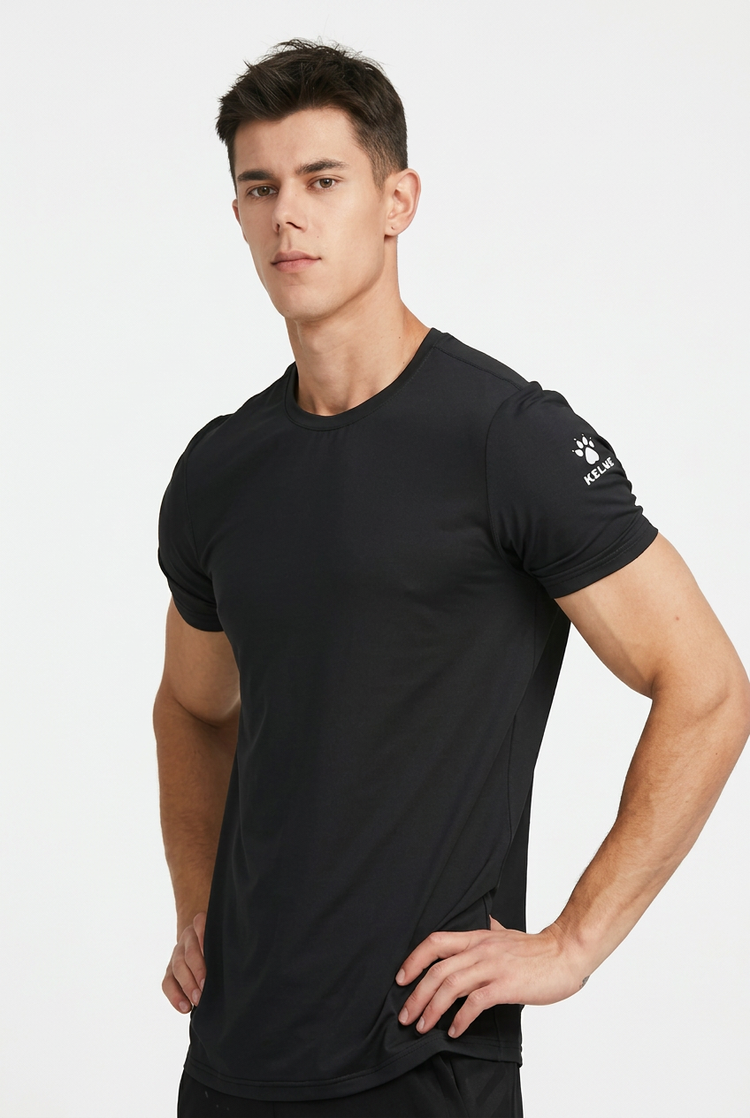 A man wearing a black short-sleeve athletic t-shirt with a small white logo on the left sleeve, photographed against a clean light gray studio background.